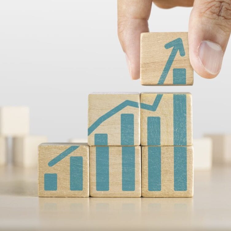 AdobeStock_243485763-sm Business growth, progress or success concept. Wooden blocks with a growing bar chart graphic arranged in stair shape and a man is holding the top one.